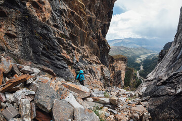 Backpacking woman climbing up on steep cliff edge at high altitude mountains top