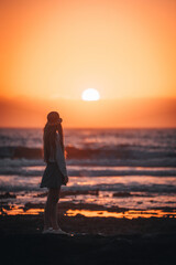 Fototapeta premium A woman stands on the beach, looking out at the sun as it sets