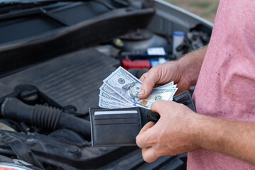 Customer taking dollar banknotes of his wallet to pay for car repair. Spending money for repair at...