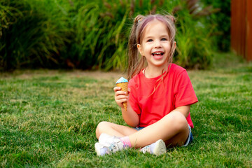 Little baby girl eating ice cream in summer on a green lawn grass, bright summer photo of a happy and laughing child with ice cream