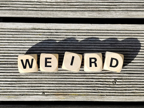 Wooden dice spelling the word weird on a wooden background