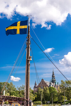 Swedish flag on a sailing ship with Nordic Museum in the background on a sunny day in Stockholm.