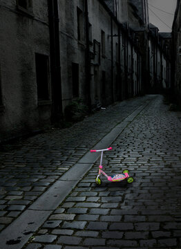 Colorful child's scooter stands alone in a drab, desolate urban street