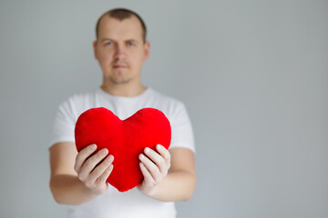 Obraz premium Man holding red heart pillow on grey background
