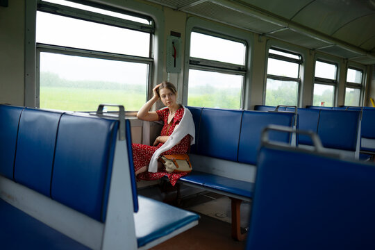 Mid adult woman sitting alone in a train compartment during daytime, looking contemplative.