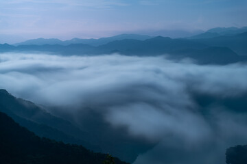 A breathtaking panoramic view of a sea of clouds below a crescent moon and a starry night sky. The silhouette of distant mountains adds depth and drama to this serene landscape. Xindian, Taiwan.