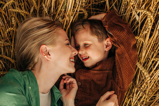 Mother and son lying on a wheat field, smiling and bonding, top view.