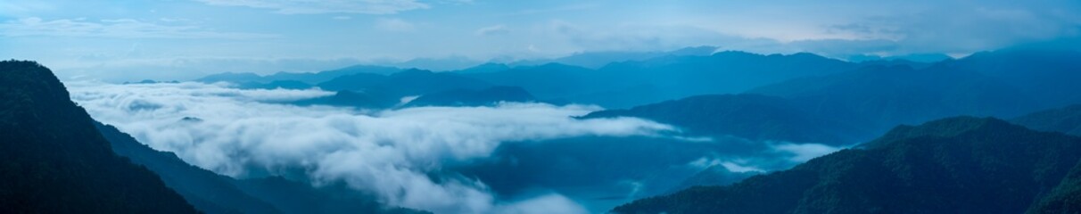 A breathtaking panoramic view of a sea of clouds below a crescent moon and a starry night sky. The silhouette of distant mountains adds depth and drama to this serene landscape. Xindian, Taiwan.