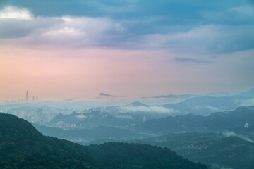 A breathtaking view of a valley shrouded in mist, with distant mountains peeking through the clouds. The lush greenery and soft, natural light create a beautiful and calming scene. Xindian, Taiwan.