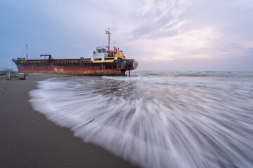 A solitary abandoned ship rests on the shore of Xigushui Beach, its weathered hull and rust-stained...