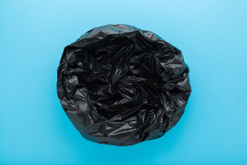 New empty dark black opened plastic garbage bag on light blue table background. Pastel color....