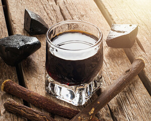 Glass of liquorice extract with pure blocks and sticks on rustic wood