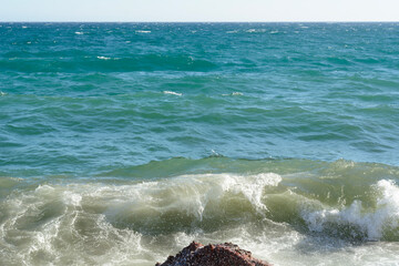 The stormy blue ocean with a wave near the stones. Windy summer day on the blue sea