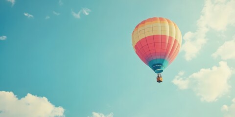 Naklejka premium A vibrant hot air balloon floats peacefully in a clear blue sky, surrounded by soft white clouds, capturing the essence of adventure.