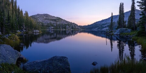 Fototapeta premium Tranquil mountain lake at dawn, reflecting colorful sky and surrounding trees, creating a peaceful natural scene.
