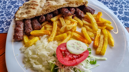 Plate of Cevapi in Mostar. Balkan dish consisting of grilled minced meat rolls. Crispy French fries and accompanied by a side salad of shredded cabbage, tomato, cucumber. Wrapped in a warm pita bread.