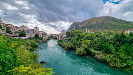 Aerial view of Old Bridge of medieval town Mostar spanning the Neretva River, Bosnia and Herzegovina. UNESCO World Heritage Site. Ancient arch stone structure on cloudy day surrounded by minarets © Chris