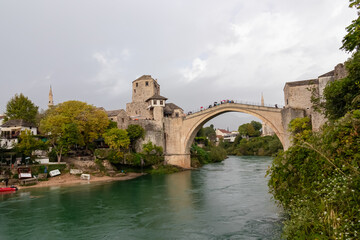 Scenic view of Old Bridge of medieval town Mostar spanning the Neretva River, Bosnia and Herzegovina. UNESCO World Heritage Site in. Ancient arch stone structure at cloudy day surrounded by minarets