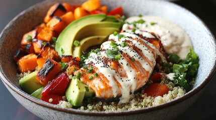 A healthy and colorful Buddha bowl filled with quinoa, roasted vegetables, avocado slices, and flaked salmon, drizzled with tahini dressing.