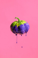 Decorative Autumn pumpkin with purple paint drips on pink background. Creative composition is perfect for fall, Halloween, or artistic-themed projects.