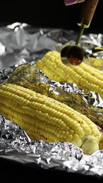 Cooking corn cobs. Preparing corn for baking. Adding spices into corn to bake it. Fresh cron cobs being spiced with chili flakes to roast in the oven