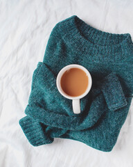 Green sweater with a cup of coffee or tea isolated on white linen background. Flat lay. Top view. Copy space