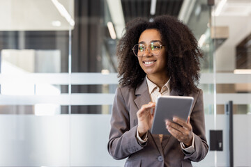A young African American woman in a business suit is standing inside an office center, holding a...