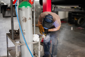 A skilled welder wearing protective gear concentrates on metalwork in a busy industrial workshop. Sparks fly as the welding process creates a vibrant display of craftsmanship and industry.