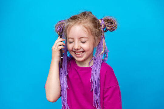 Happy little girl in pink t-shirt talking on phone and laughing on blue background. Child using modern smartphone. Copy space, high quality photo. Conversation concept.