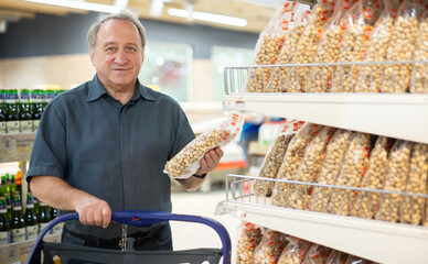 Mature man carefully reads date of packaging of pistachios in the grocery section of supermarket