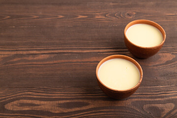 Organic non dairy banana and soy milk in clay cup on brown wooden, side view, copy space.