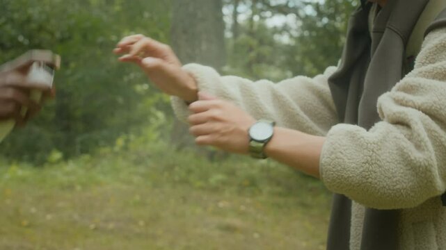 Slowmo closeup of hikers applying mosquito repellent spray on skin while standing on forest trail and getting ready for summer hiking trip