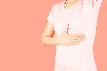 Woman palpating her breast by herself isolated on pink background. Breast self-exam for breast cancer awareness concept.