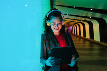 Young woman using tablet and wearing headphones in urban tunnel at night