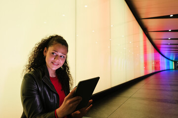 Young woman is using tablet and sitting in colorful tunnel