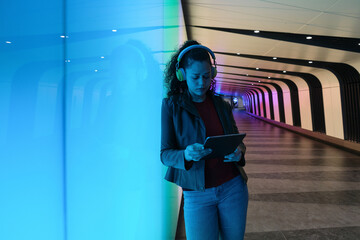 Young woman using digital tablet in a modern urban tunnel with neon lights