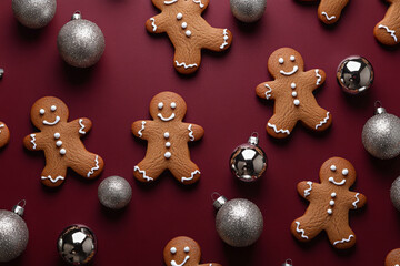 Capture an overhead perspective of gingerbread men cookies artfully arranged on a deep burgundy background, interspersed with shimmering silver Christmas ornaments. The colors create an elegant and