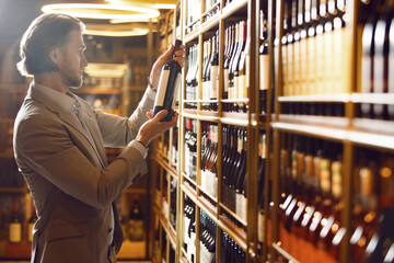 Experienced sommelier taking one of bottles from wooden shelf standing in wine cellar