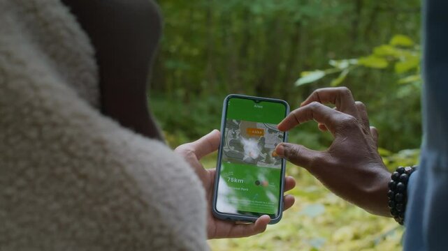 Over shoulder of couple of tourists using navigation app in smartphone while getting lost in lush forest during hiking trip