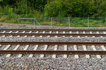 Parallel train track horizontal shot. Wire fence protected, pedestrian footpath and green nature in the background, no people