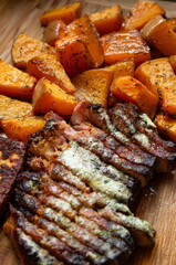 Home made, oven roasted and seasoned pumpkin next to slices steak with melting butter. Close up shot, top view, no people