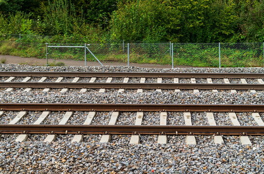 Parallel train track horizontal shot. Wire fence protected, pedestrian footpath and green nature in the background, no people