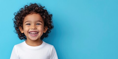 a happy, laughing child with curly hair, wearing a white t shirt against a blue background