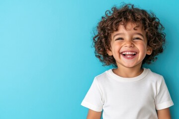 a happy, laughing child with curly hair, wearing a white t shirt against a blue background