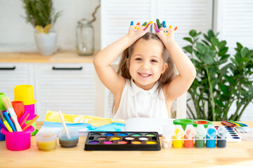 a small child, a girl with painted hands in paints, learns to draw by playing, a girl plays around...