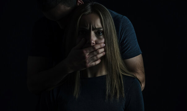 Terrified woman being silenced by a man in a dark setting, representing fear, control, and the grim reality of abuse and domestic violence