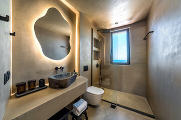 Modern bathroom interior design with cave-like in beige tones.  stone-like sink with natural...