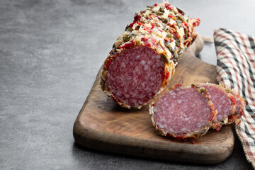 Dry-cured sausage sprinkled with spices and herbs on wooden board