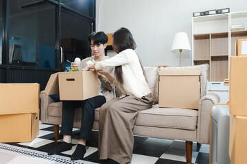 Young couple relaxing sitting on the sofa using the computer laptop around cardboard boxes, very happy moving to a new house.