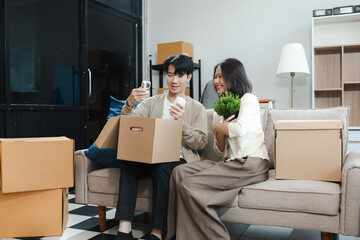 Young couple relaxing sitting on the sofa using the computer laptop around cardboard boxes, very happy moving to a new house.